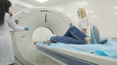 Kadın hasta, modern tıp kliniğinde iki kalifiye radyoloğun gözetiminde CT veya MRI taramasından geçiriliyor. Tomografide veya MR tarama masasında yatan hasta, makinenin dışına çıkıyor.