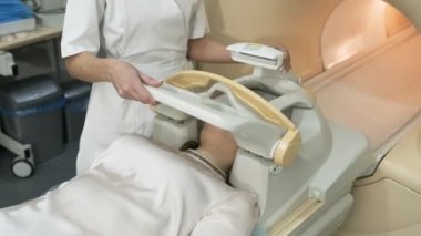 Kadın radyolog beyin, kafa ve boyun MR taraması yapıyor. Otomatik masadaki genç bayan hasta, modern ekipmanlarla kapalı bir MRI makinesine giriyor, hastanın kafasına dolanıyor..
