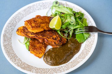 Tavuk eti kaplama ve hamurda kızartma, patlıcan sosu ve açık mavi arka planda limonlu taze yeşil salata yaprağı, yakın plan..