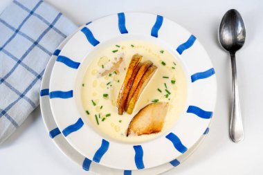 Kuşkonmaz çorbası, beyaz tabakta kızarmış elma parçaları, mavi çizgili, kaşık ve mavi havluyla beyaz arka planda, yakın plan..