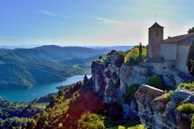 Santa Maria de Siurana 'nın Romen kilisesi kayanın tepesinde, vadiye bakan, arka planda dağlar. Beyaz bulutlu mavi gökyüzü. Siurana, Katalonya, İspanya.