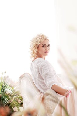 Çekici genç bir kadın kanepede oturuyor. Bahar dekoru. Yumuşak ışık.