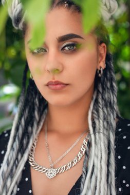 Ağaçların yaprakları arasında uzun beyaz rastalı güzel bir kadının portresi. Yaz zamanı, gün ışığı.