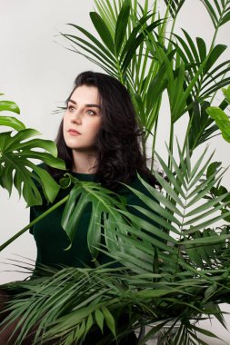 Genç ve güzel bir kadın büyük ev bitkilerinin arasında oturuyor..