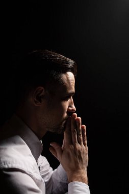 Dua eden yakışıklı sakallı adam. Düşük ışık portresi. Siyah arkaplan.