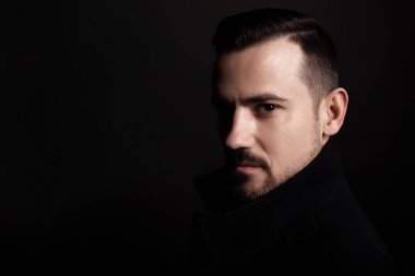 Siyah paltolu yakışıklı sakallı adam. Siyah arkaplan.