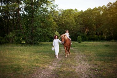 Anne ve kızı ata biniyor. Yaz zamanı..