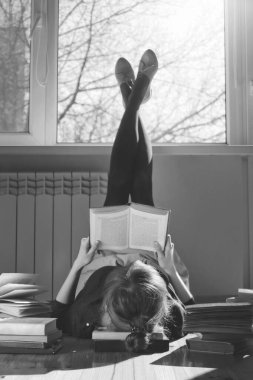 Genç bir kadın yerde uzanıyor ve kitap okuyor.