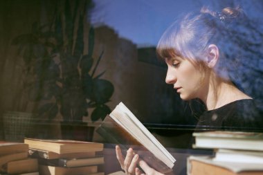 Genç bir kadın yerde oturup kitap okuyor.