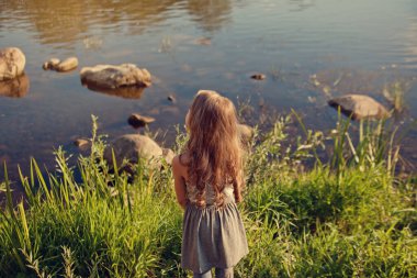 Küçük kız özenle nehre bakıyor.  