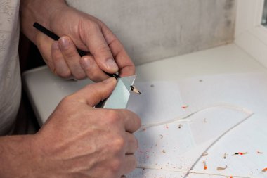 Man sharpens black pencil for drawing with a knife.