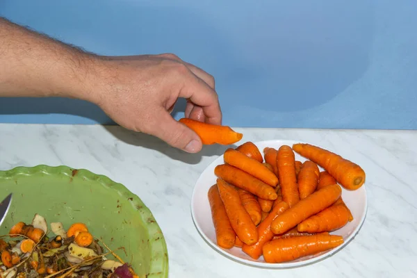 Un hombre limpia zanahorias y las pone en un plato donde ya hay muchas zanahorias — Foto de Stock