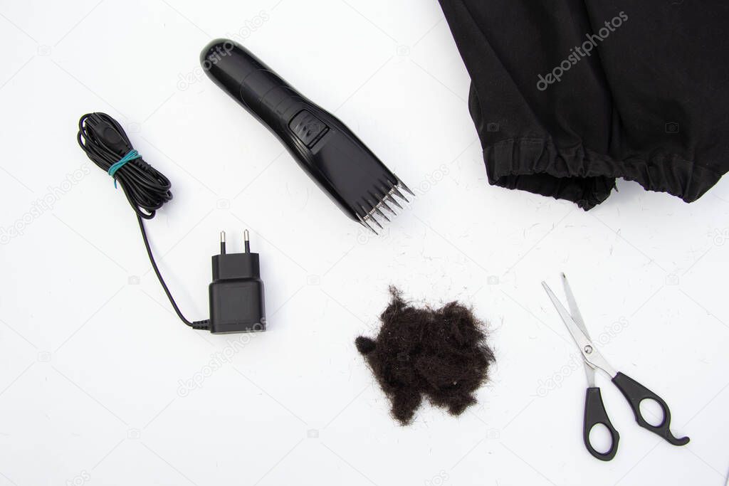 a bunch of cut black hair, a haircut machine, scissors, a black cape on a white background. View from above.