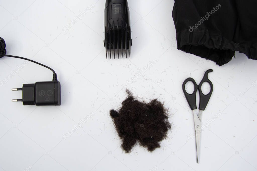 Haircut accessories: comb, typewriter, cape, black hair. View from above, background white.