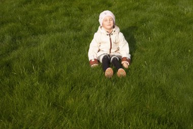 Altı yaşında bir kız gözlerini kapatan yeşil çimlerin üzerinde mutlu bir şekilde oturur..