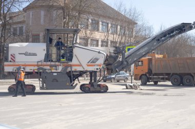 Şehirde asfalt fırlatan büyük bir makine açılıyor. Yakınlarda bir çöp kamyonu var. Yol kesiciler.