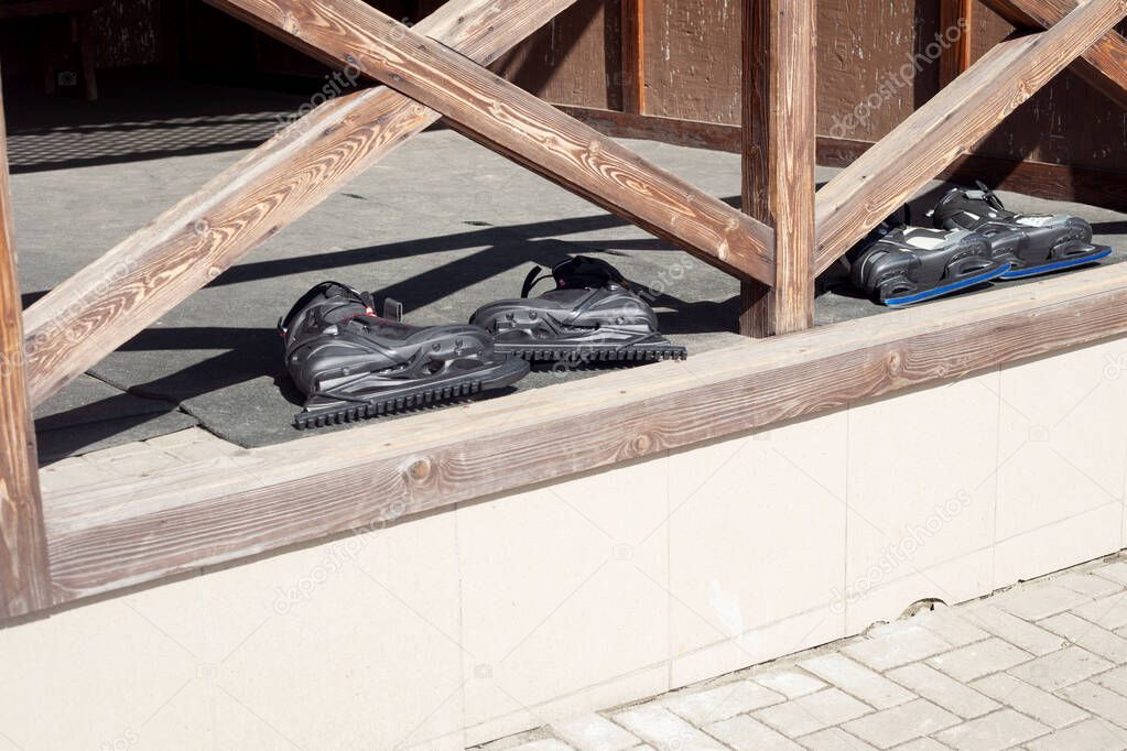 Two pairs of black skates lie on a wooden terrace. The end of skating season