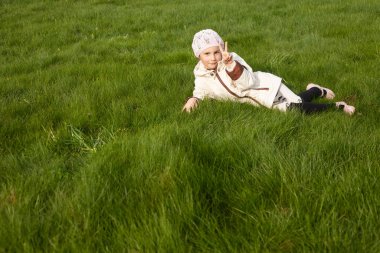 Parlak çimenlerin üzerinde ceketli mutlu ve neşeli bir kız yatıyor.