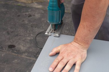 Erkeklerin elleri testereyi tutuyor. Elektrikli testereyle küçük bir kontraplak oyması.