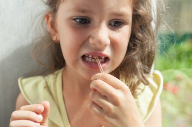 Anaokulundan bir kız ipleri elinde tutuyor. İplik süt dişine bağlanmış. Evde diş çektirme..