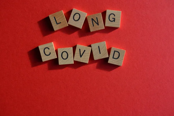 Long Covid, ahşap alfabe harfleriyle yazılmış kelimeler. Parlak kırmızı arkaplanda izole edilmiş ve kopyalama alanı olan kelimeler.
