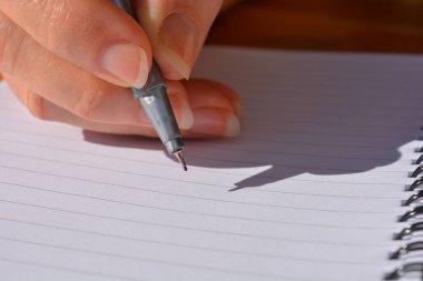 Elinde kalem, sarmal bağlı defterin boş sayfası üzerinde duruyormuş.