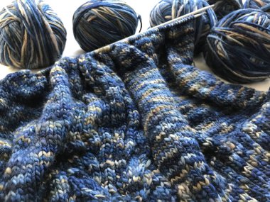 Örgü iğneleri, yün yumakları ve mavi örgü kazağın bir parçası.