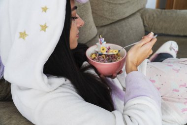 Tek boynuzlu at kürklü genç bir kadın kahvaltıda renkli mısır gevreği ve portakal suyu yiyor.