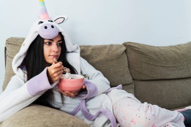 Tek boynuzlu at kürklü genç bir kadın kahvaltıda renkli mısır gevreği ve portakal suyu yiyor.