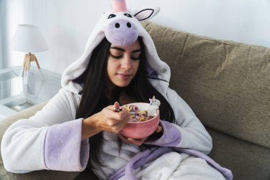 Tek boynuzlu at kürklü genç bir kadın kahvaltıda renkli mısır gevreği ve portakal suyu yiyor.