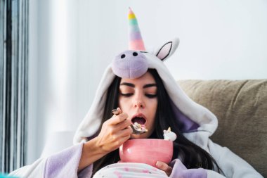 Tek boynuzlu at kürklü genç bir kadın kahvaltıda renkli mısır gevreği ve portakal suyu yiyor.