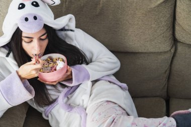 Tek boynuzlu at kürklü genç bir kadın kahvaltıda renkli mısır gevreği ve portakal suyu yiyor.