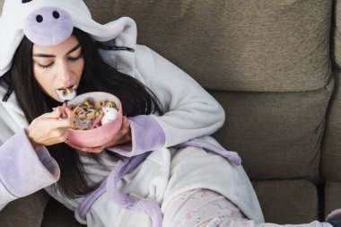 Tek boynuzlu at kürklü genç bir kadın kahvaltıda renkli mısır gevreği ve portakal suyu yiyor.