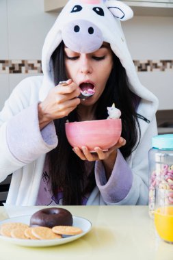 Tek boynuzlu at kürklü genç bir kadın kahvaltıda renkli mısır gevreği ve portakal suyu yiyor.