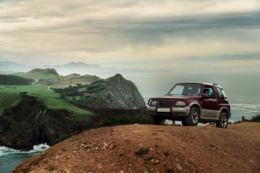 Bir tepenin üstünde, çarpıcı bir gökyüzü olan güzel bir sahil manzarası olan off road car.
