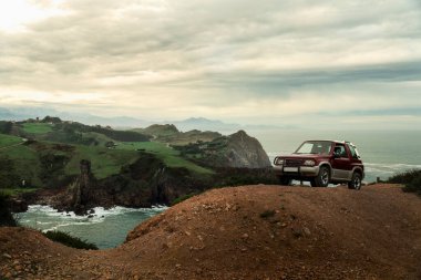 Bir tepenin üstünde, çarpıcı bir gökyüzü olan güzel bir sahil manzarası olan off road car.