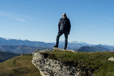 60 yaşındaki bir adam Kuzey İspanya 'da bir dağ yürüyüşünden sonra poz veriyor. Arka planda güzel bir doğa manzarası var.