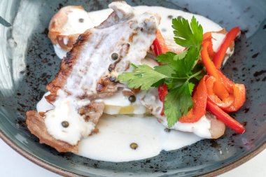 Biber soslu, maydanozlu ve sebzeli koyu mavi bir tabakta İber sırrı.