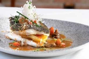 Sebze ve sığır suyu ile ızgara turbot, deniz ürünleri eriştesi ile süslenmiş, beyaz masa örtüsü ve tuğla arka planı ile