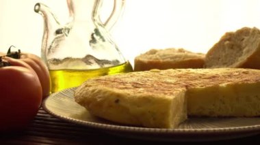 Domatesli İspanyol tortillası, sarımsak, ekmek, soğan ve açık arkaplanda bir kavanoz zeytinyağı.
