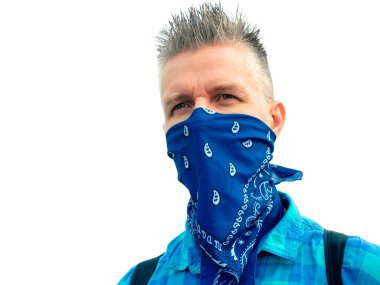 Beyaz arka planda beyaz bir adamın portresi (izole). Yüzü mavi bir bandana ile kaplıydı, mavi bir gömlek giymişti. Adamın siyah bir sırt çantası var. Yukarı doğru taranmış gri saçlar..
