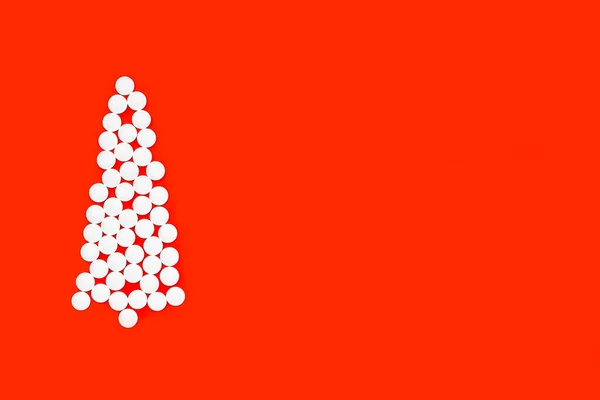 Kırmızı arka planda beyaz haplardan yapılmış noel ağacının düzlüğü, boşluğu kopyala