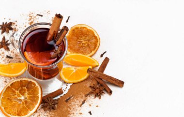 Hafif arka planda taze ve kurutulmuş portakallar, tarçın çubukları ve yıldız anasonlu bir bardak sıcak şarap. Fotokopi alanı ile çerçevele. Sıcak şarap takımlarından biri..