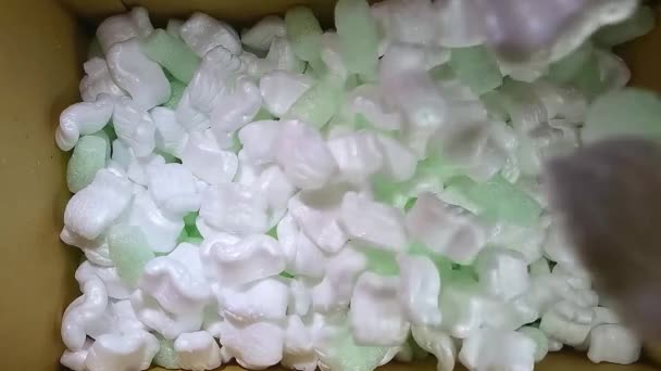 Grönt skumgummi och vitt styrofoam fyllmedel faller i en pappkartong — Stockvideo