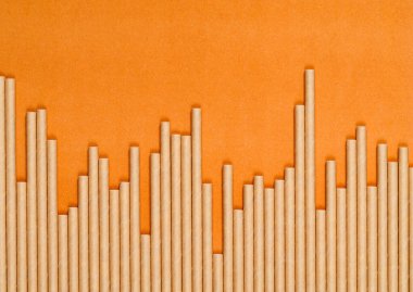Turuncu kağıt arka planda farklı yükseklikteki kağıt kokteyl pipetleri