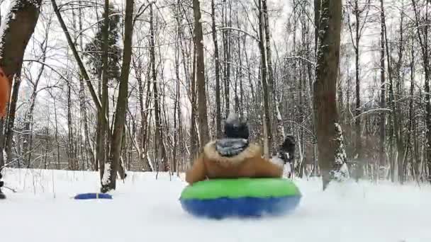 少年は冬の公園でチューブを転がしチューブはカメラの上を飛んで後ろから見る — ストック動画