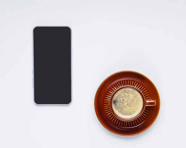 Flat lay of brown cup of black coffee and phone on white background, isolated — Stock Photo, Image