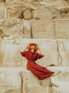 Kırmızı elbiseli ve şapkalı beyaz bir kadın Giza 'da güzel bir Khafre piramidinde oturuyor.