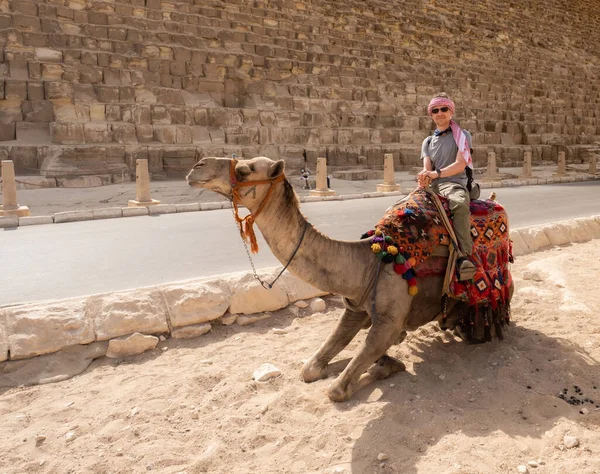 Bir turist devenin üstünde Giza 'daki piramitlerin arka planında poz veriyor.
