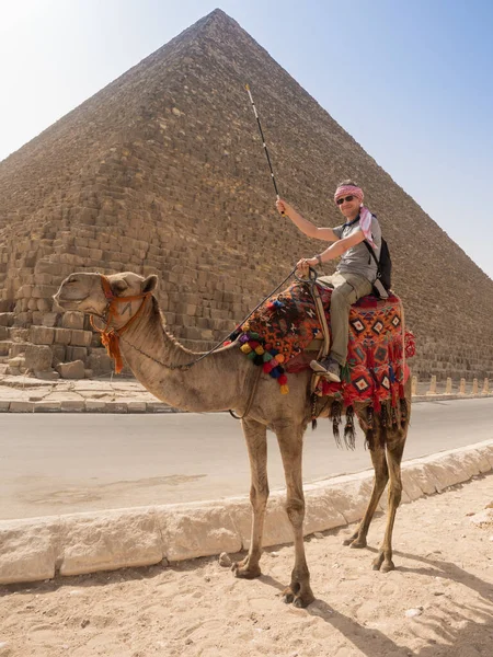 Bir turist devenin üstünde Giza 'daki piramitlerin arka planında poz veriyor.